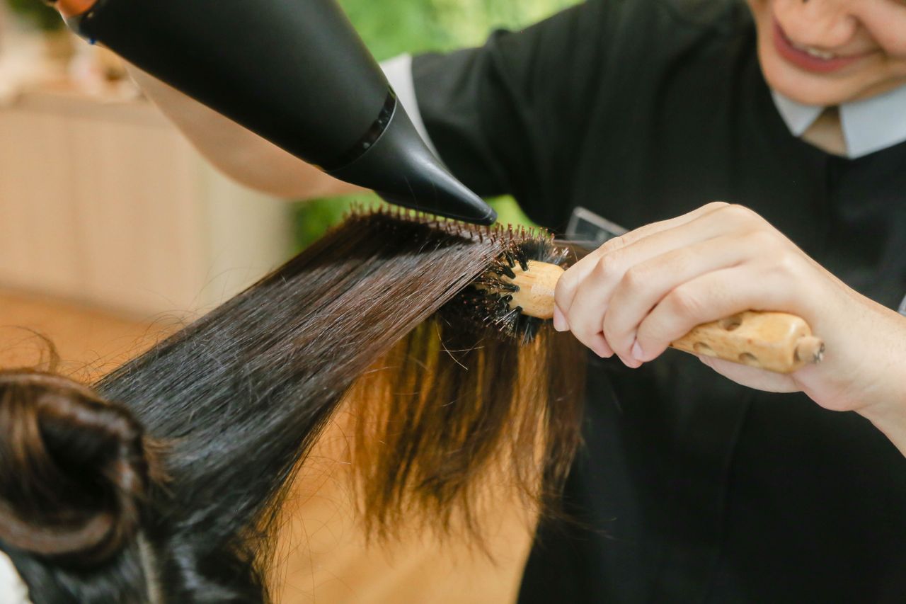 Stylist smoothing long dark hair with a round brush and dryer