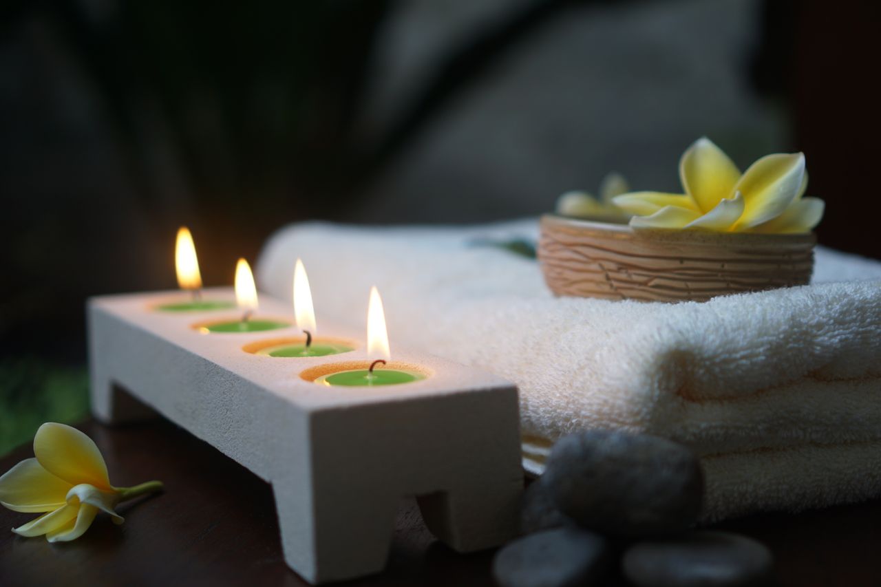 Lit candles, frangipani flowers and folded towels on a spa table